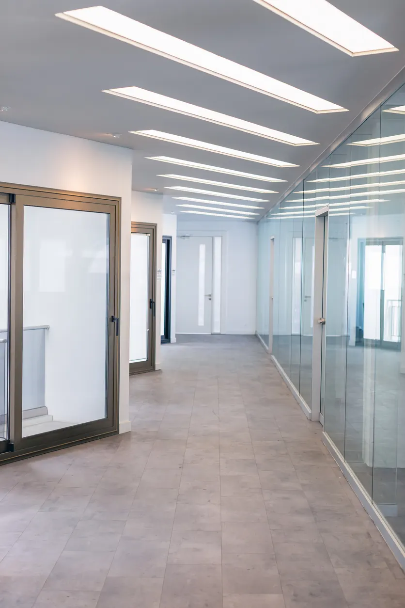 Office corridor fit-out with glazed partitions, linear ceiling lights and a porcelain floor