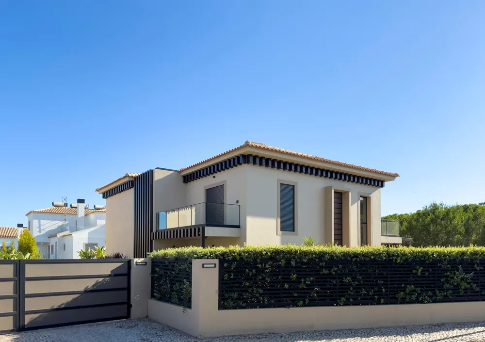 Corner view of a finished two-storey villa with dark timber screens, a planted boundary wall and a sliding gate